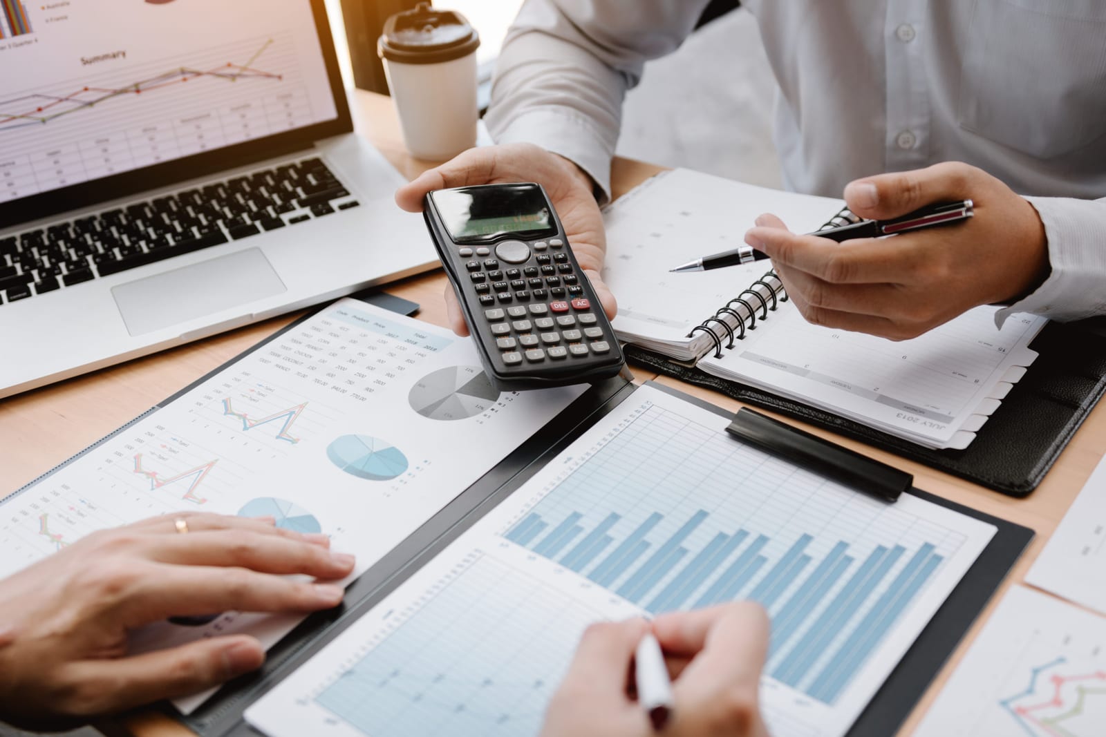 Mãos de instrutora sobre uma prancheta com planilha de custos e uma calculadora ao lado, mesa de recepção do estúdio