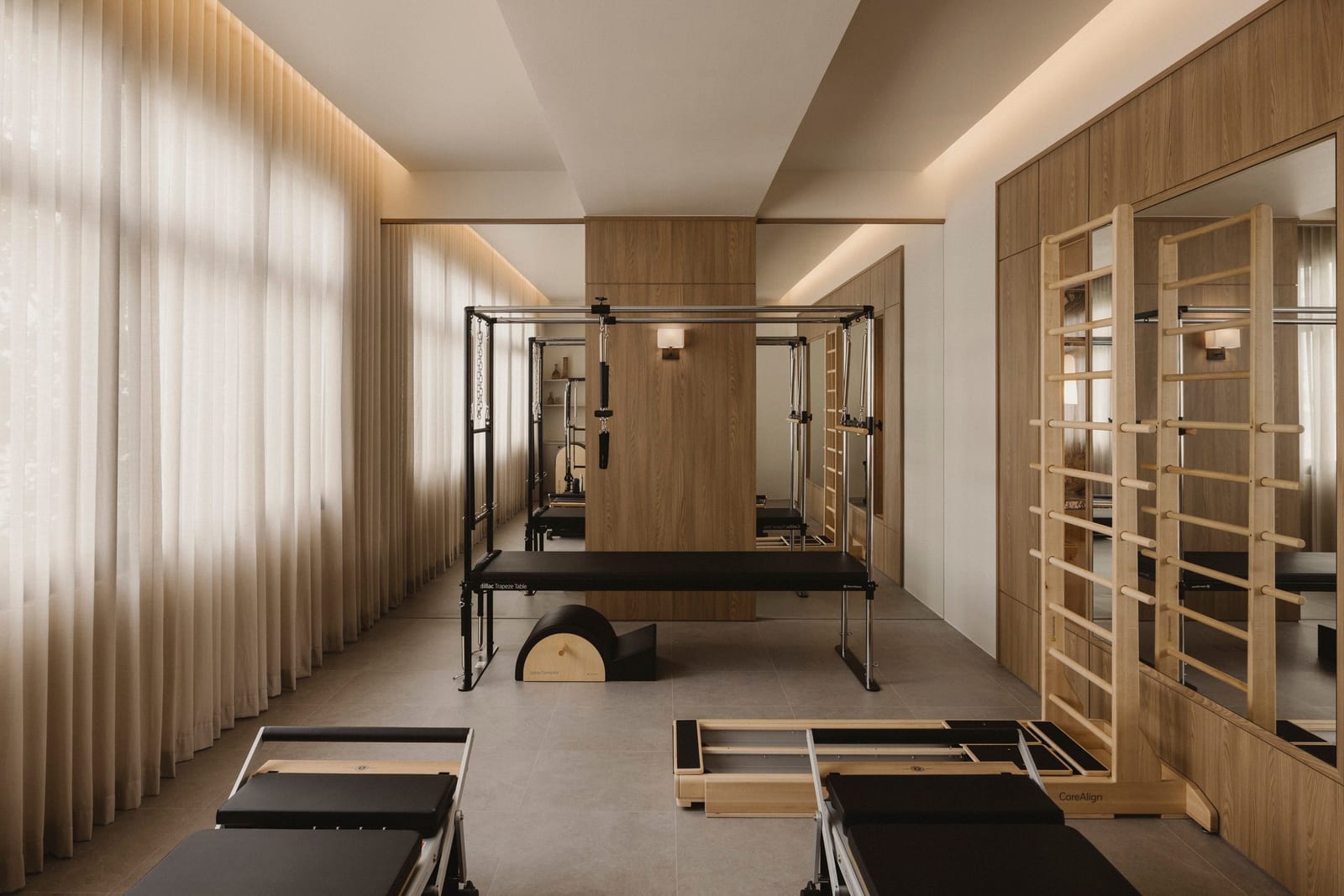 Interior de um estúdio de Pilates premium, com Cadillac, espaldar e reformers sob luz suave.