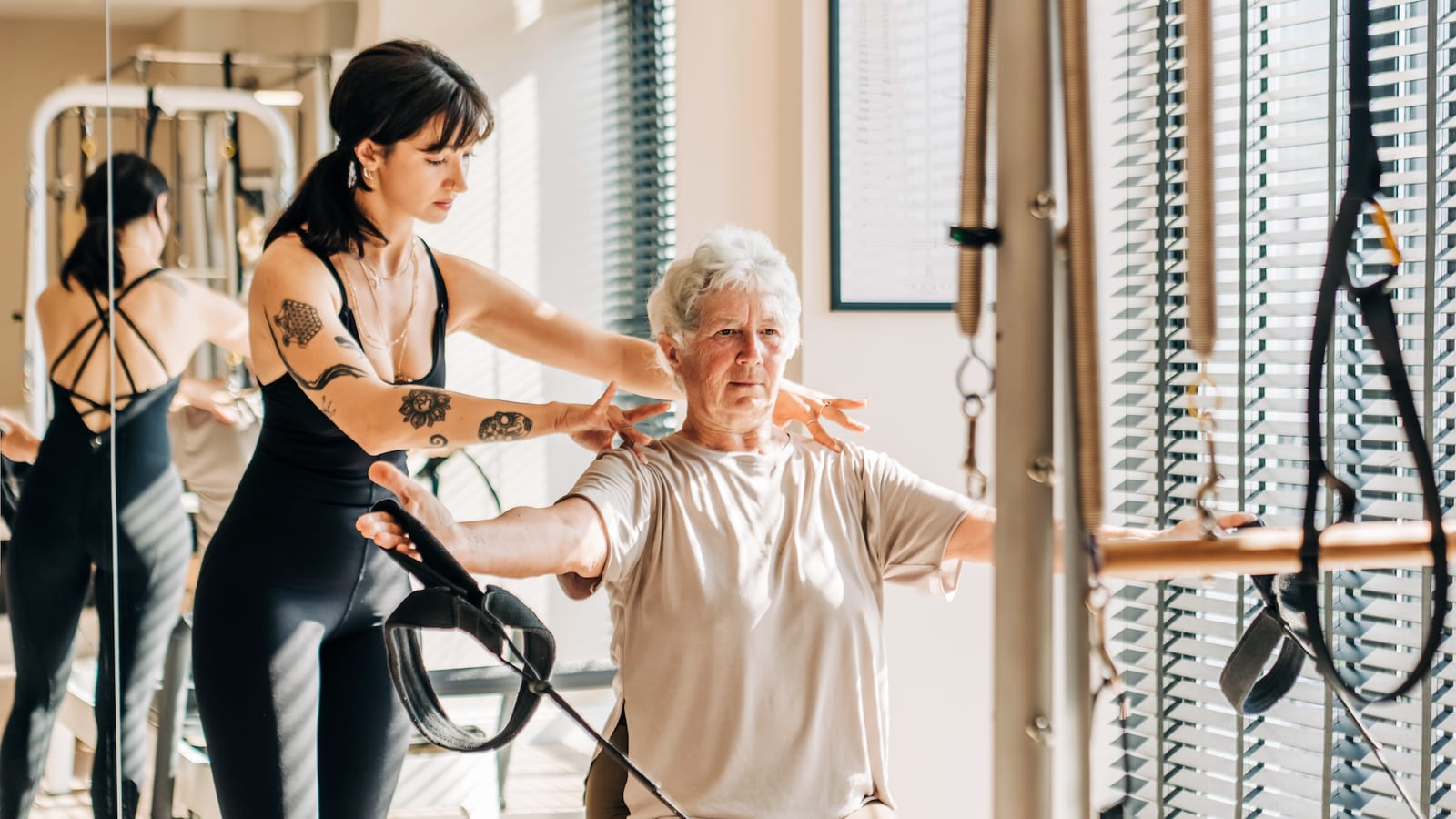Instrutora orienta de perto um aluno mais velho durante uma aula individual de Pilates